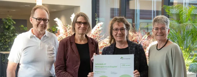 Quatre personnes se tiennent dans un espace intérieur lumineux et présentent un chèque de don lors d’une remise de don. 