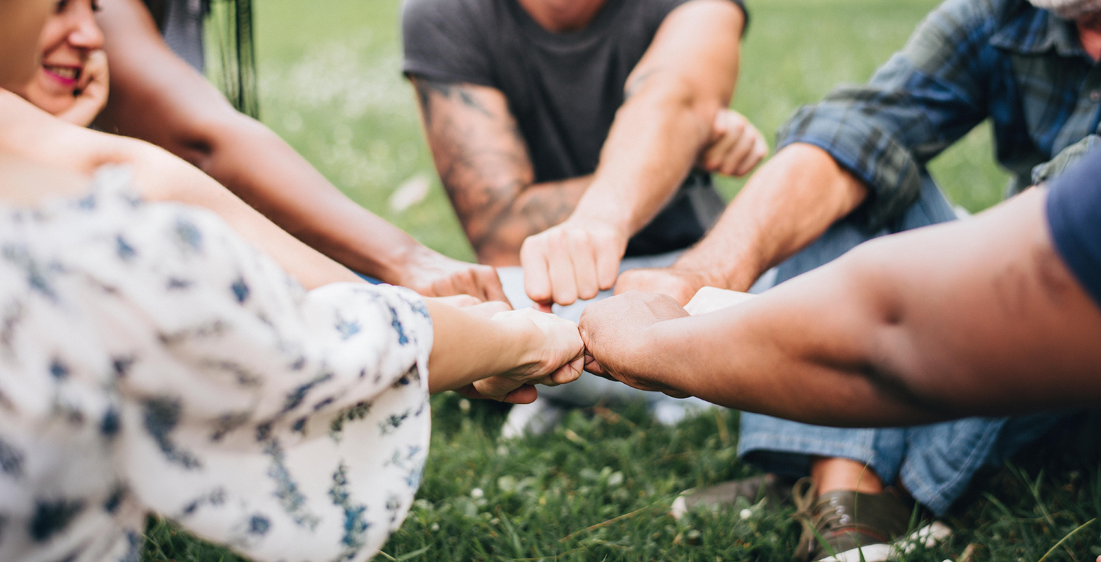 Draussen im Gras sitzenden Menschen machen einen Faustschlag