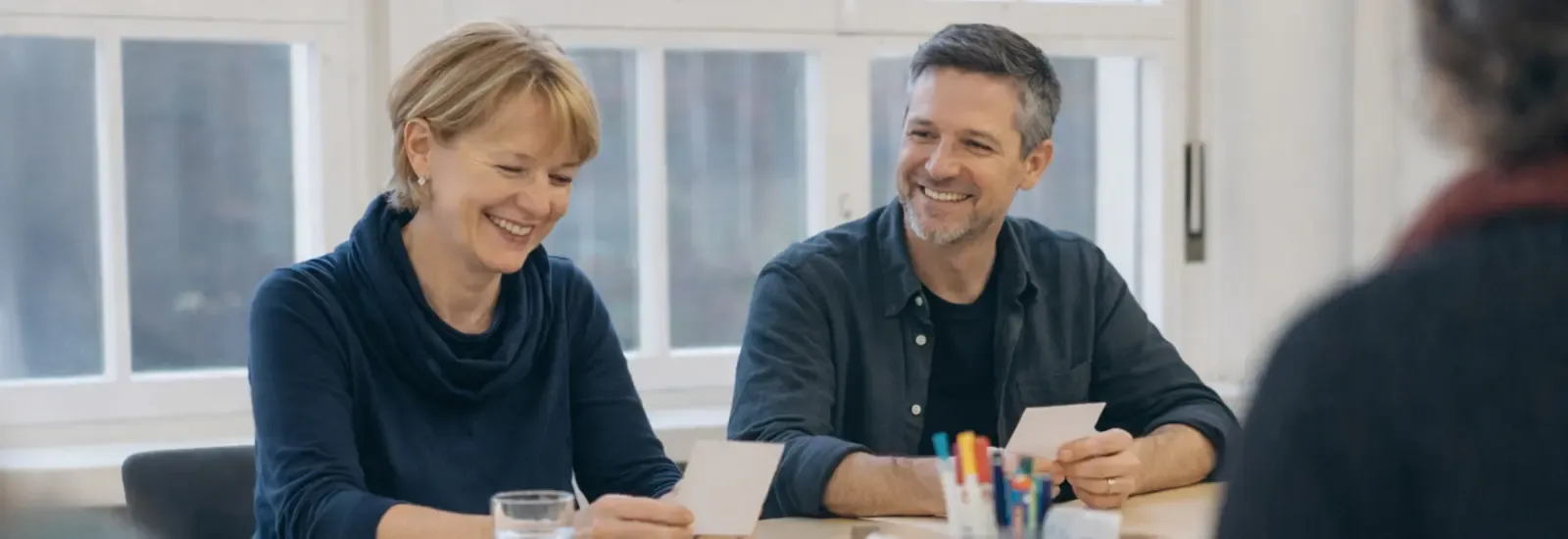 Deux membres souriants d'un groupe d'entraide sont assis à une table et regardent des cartes lors d'un échange.